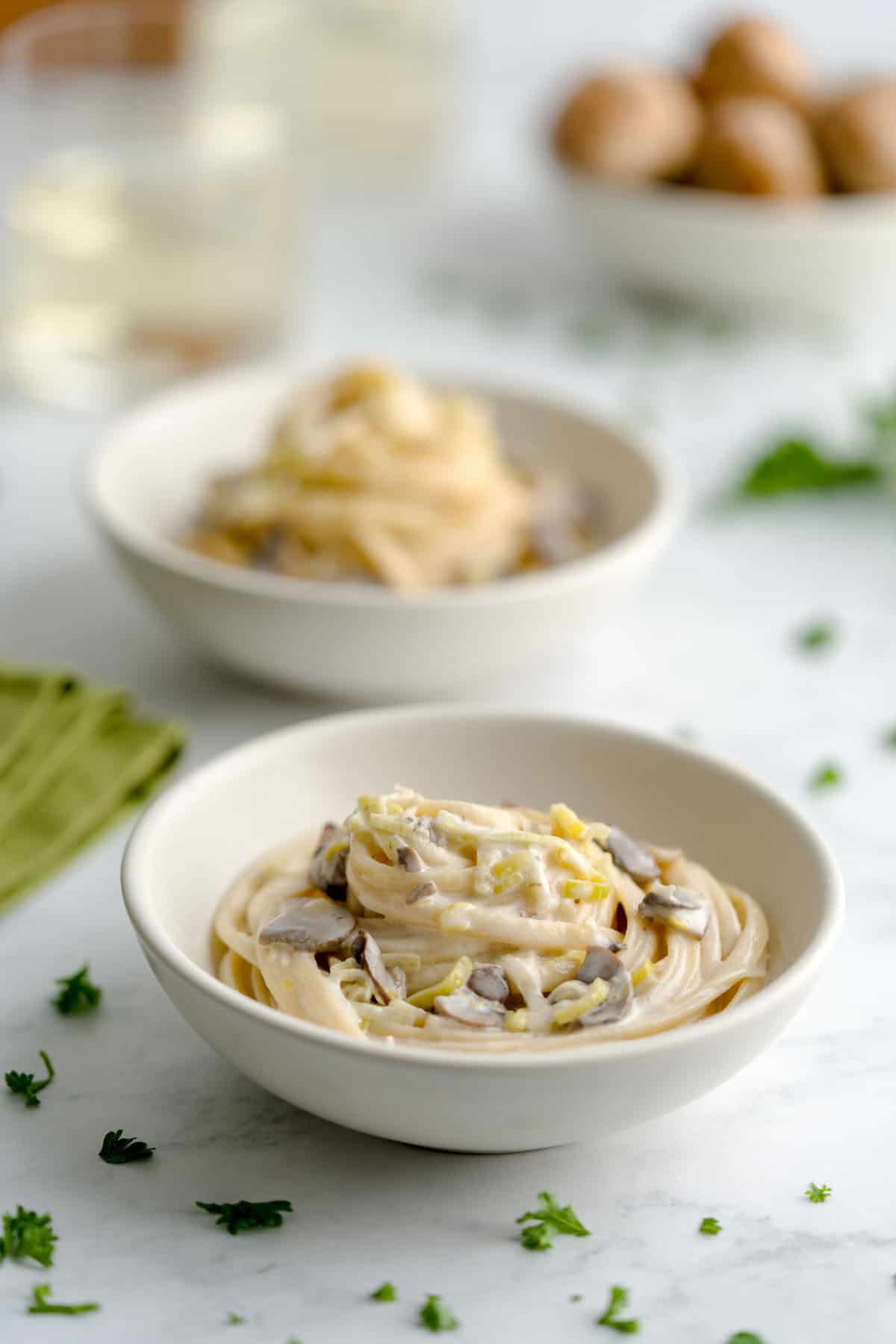 Two bowls of creamy leek and mushroom pasta next to a green cloth napkin.