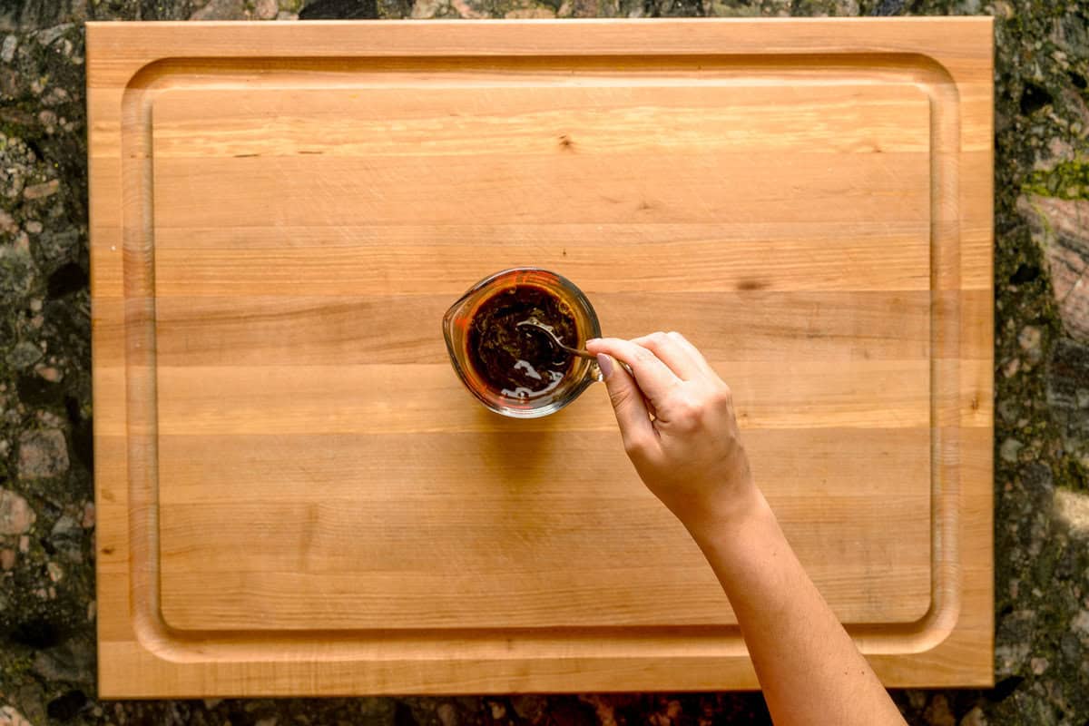 Overhead shot of a hand dissolving instant coffee into warm water in a measuring cup.
