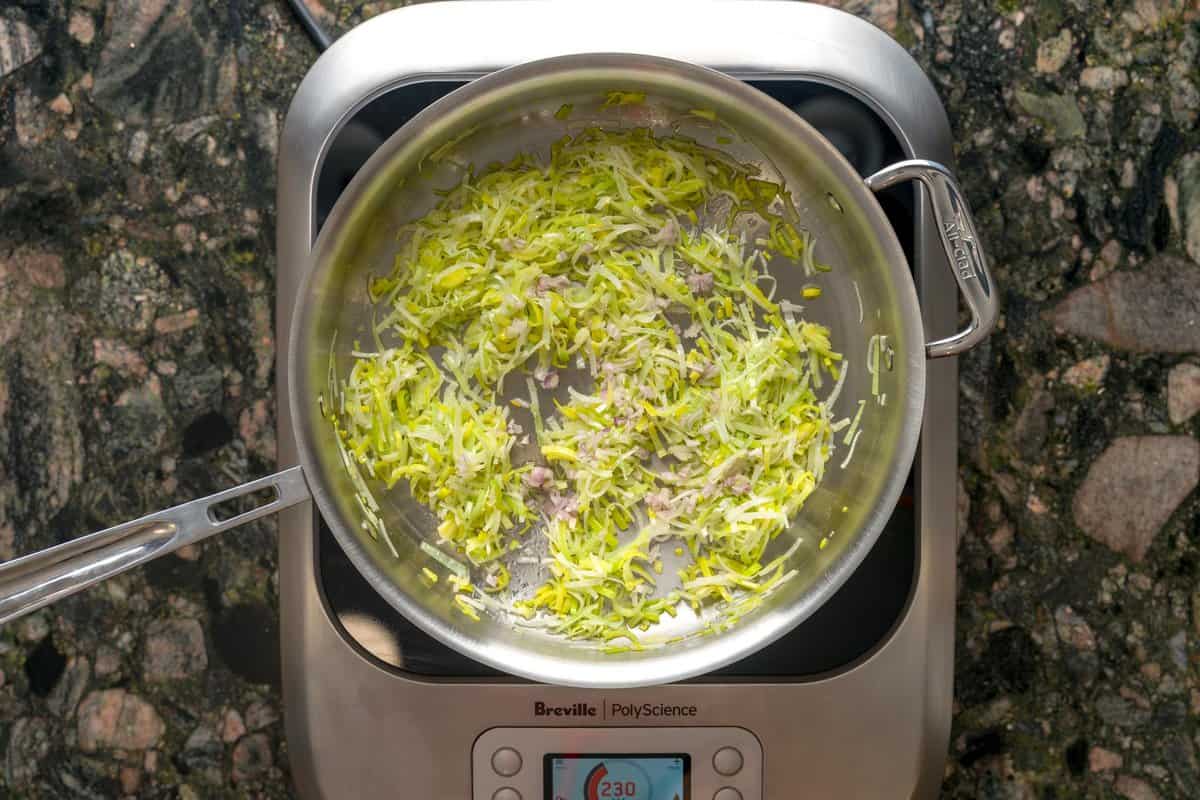 Large pan over an induction burner sautéing leeks and shallots.