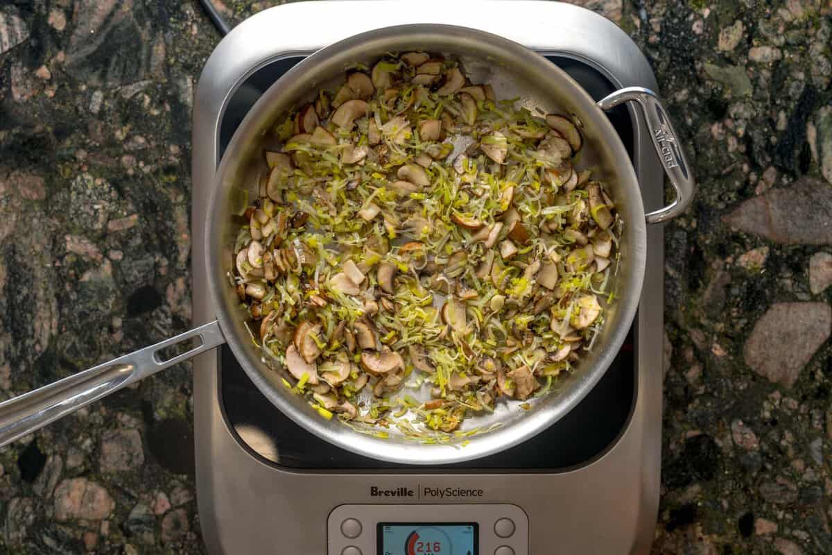 Large pan over an induction burner sautéing leeks and mushrooms.