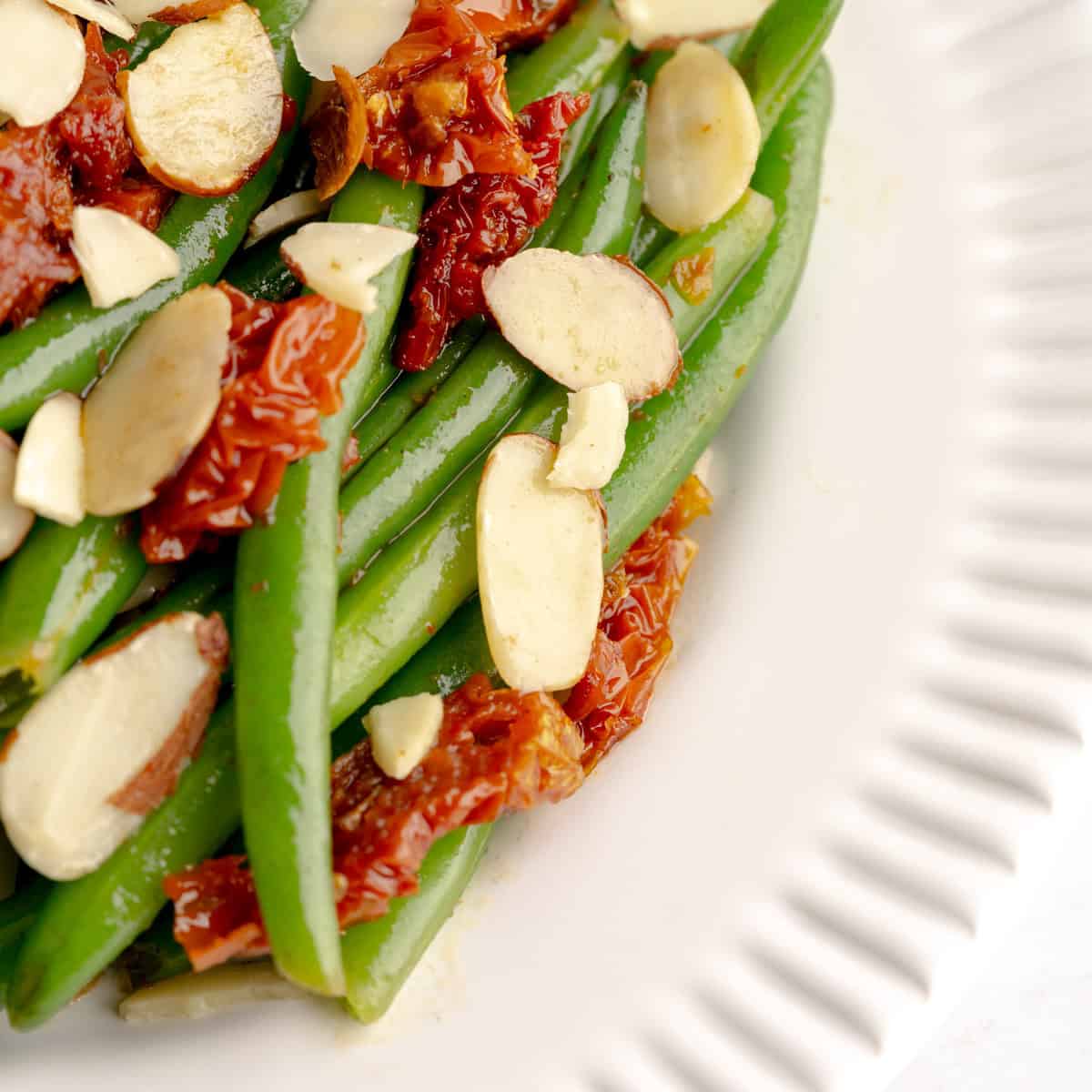 Sautéed green beans with sun-dried tomatoes and sliced almonds served on a white plate.