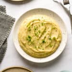 Overhead shot of creamy mashed potatoes served on a plate next to empty plates and a cloth napkin.