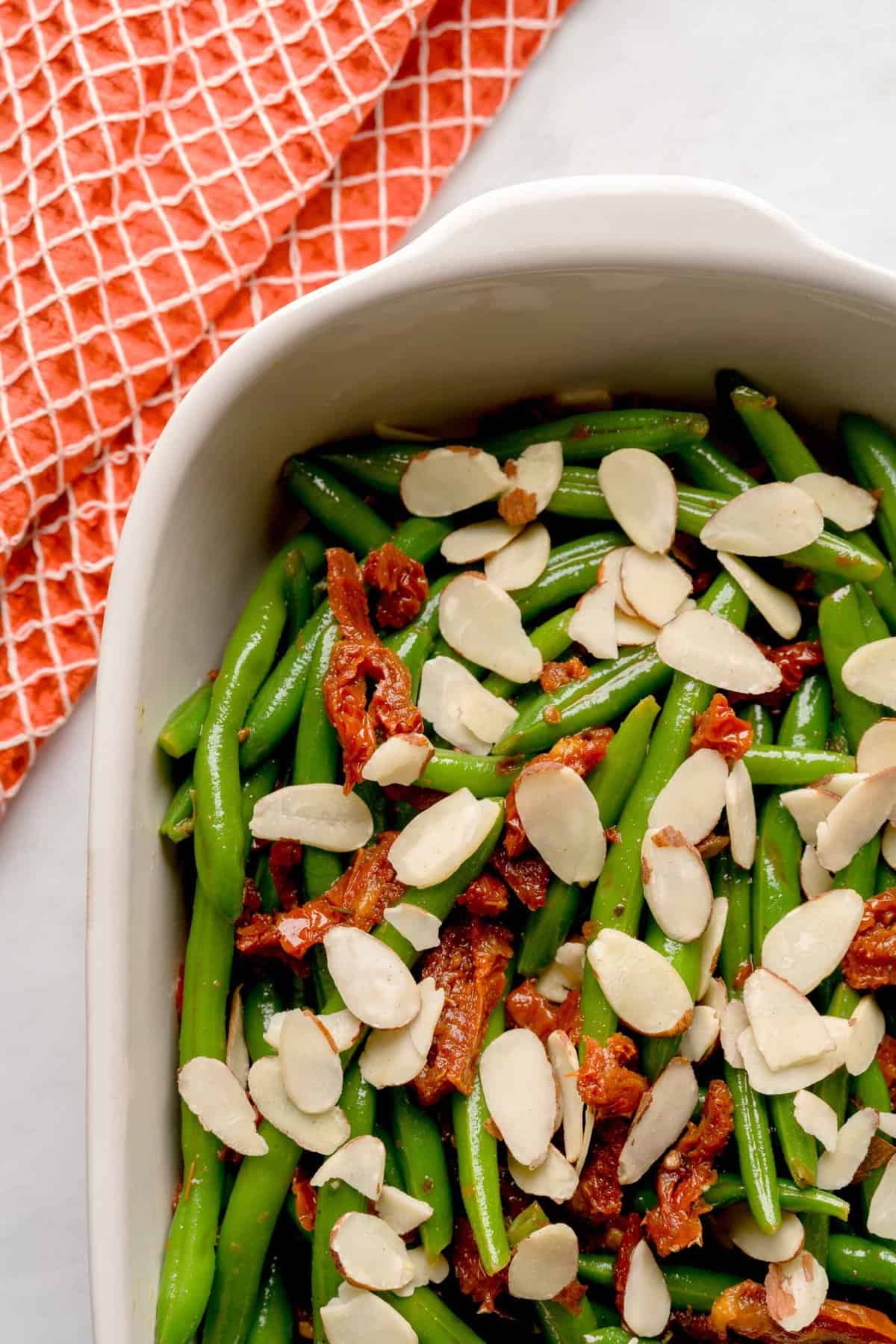 Overhead shot of Italian green beans in a serving bowl with sliced almonds and sun-dried tomatoes.