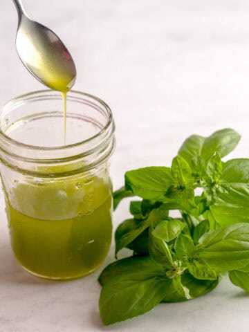 Spoon pouring basil olive oil into a jar while next to fresh basil.