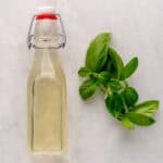 Overhead shot of bottle full of basil simple syrup next to fresh basil.