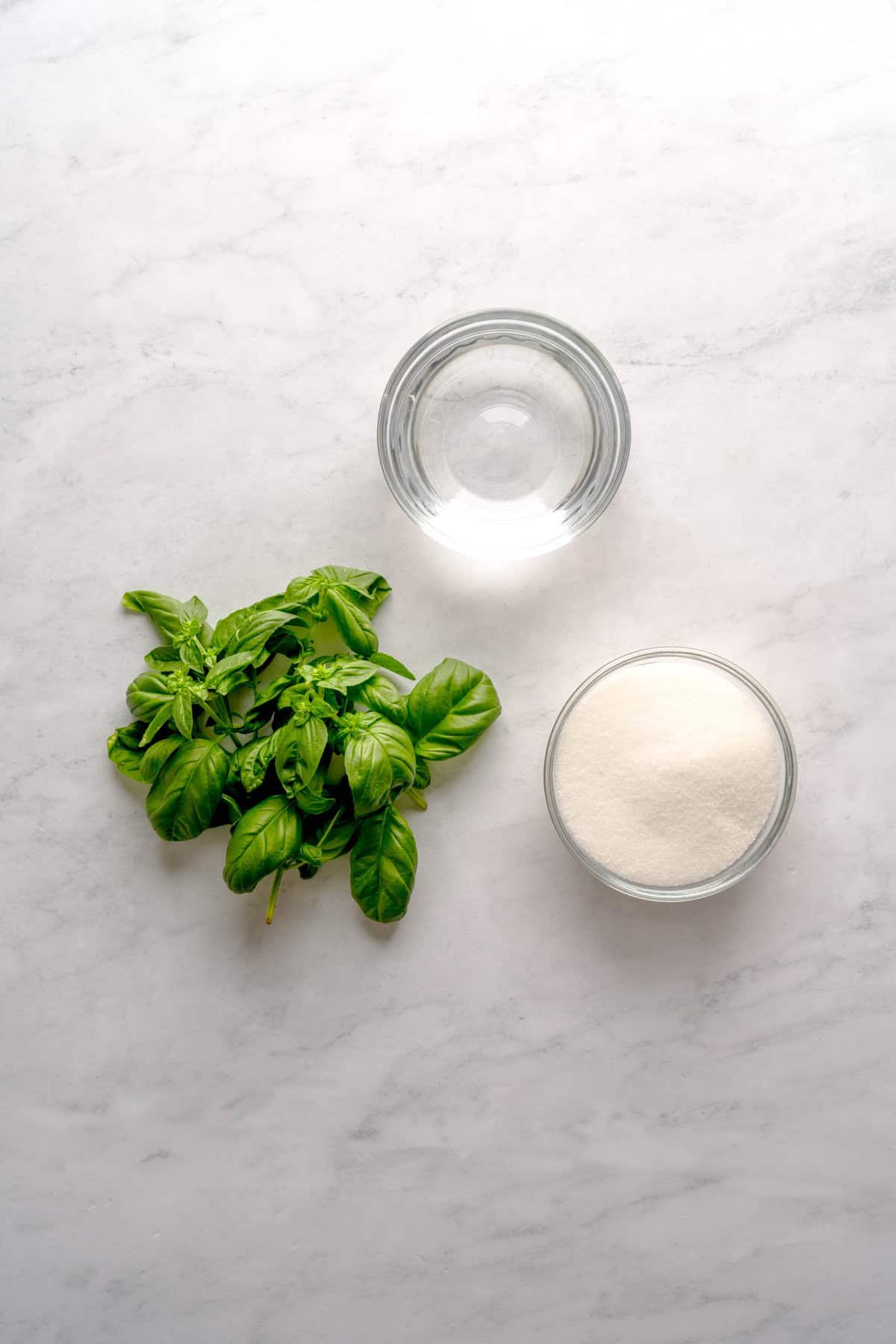Overheard shot for ingredients to make basil simple syrup, including fresh basil, water and granulated sugar.