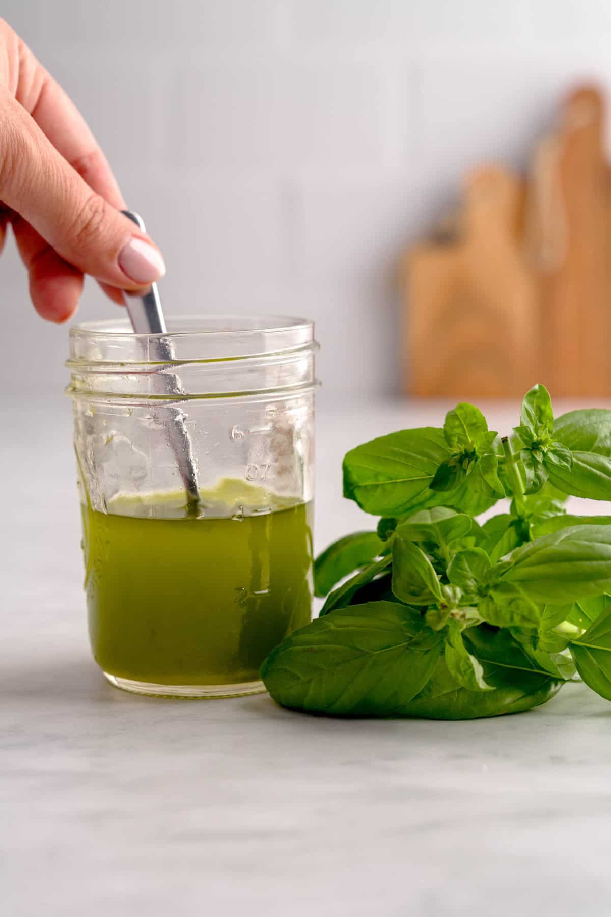 Basil oil in a jar next to fresh basil.