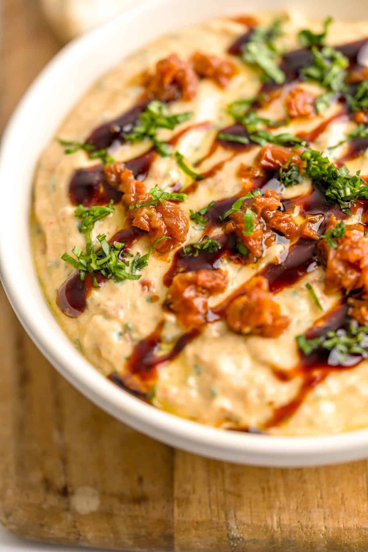 Close up shot of a bowl of whipped ricotta dip with sun-dried tomatoes and basil drizzled with balsamic glaze.