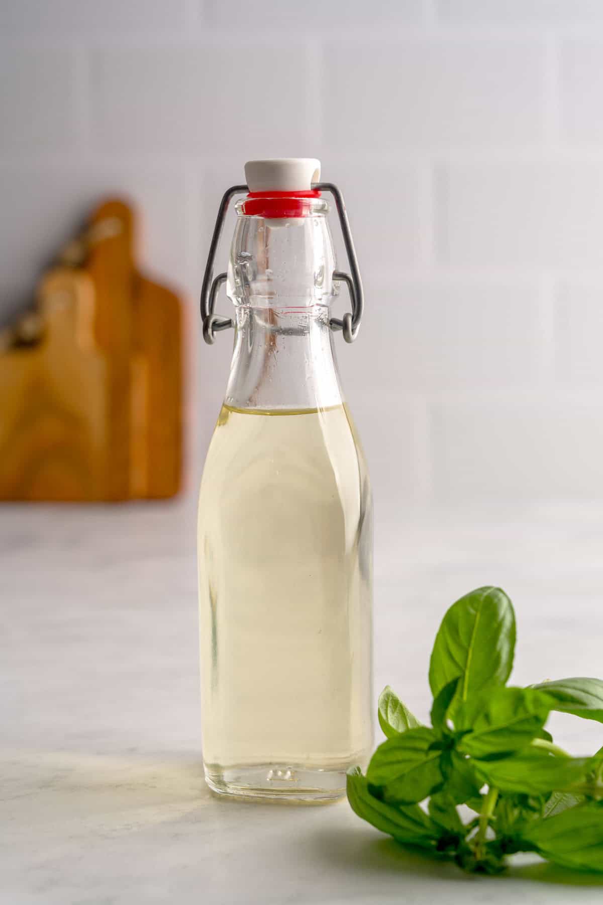Glass bottle full of basil simple syrup next to fresh basil.