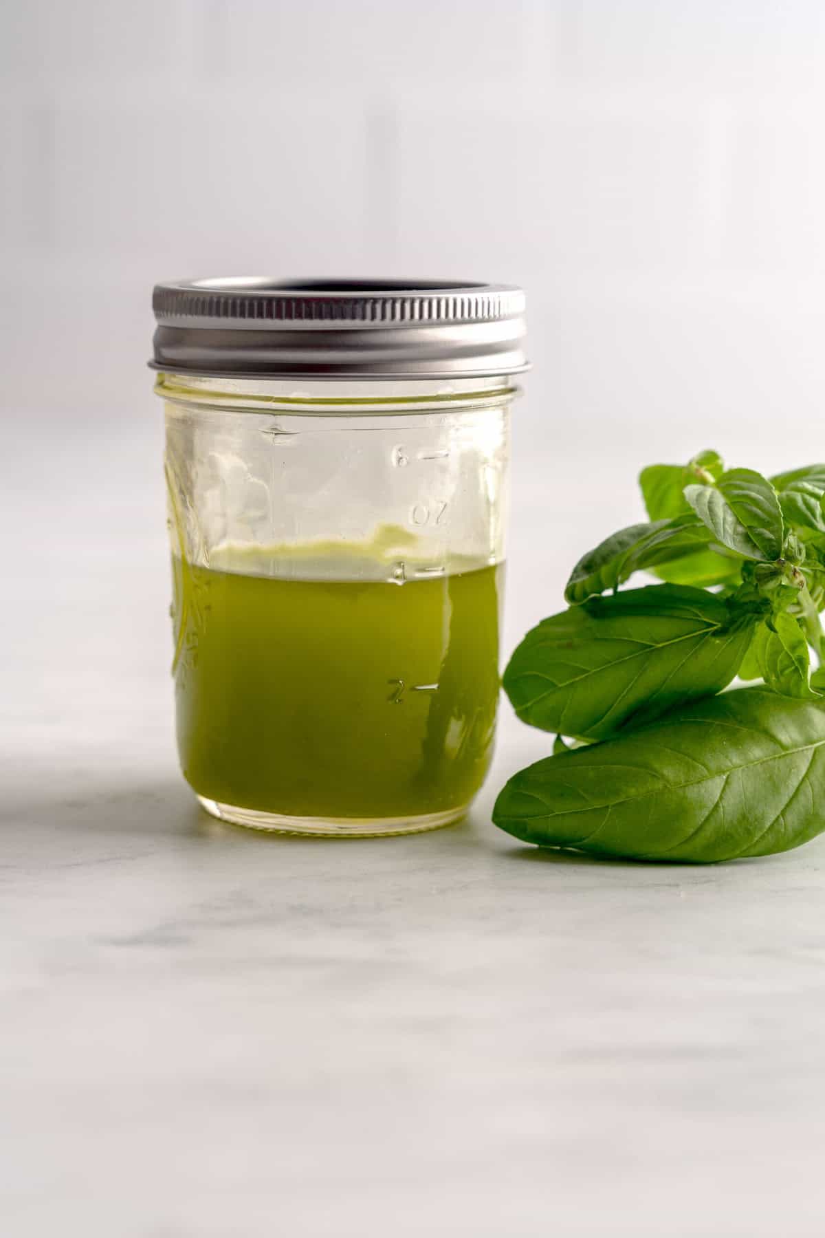 Jar of homemade basil oil next to fresh basil.