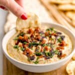 Dipping a pita bread cracker into a bowl of whipped ricotta dip with sun-dried tomatoes and basil.