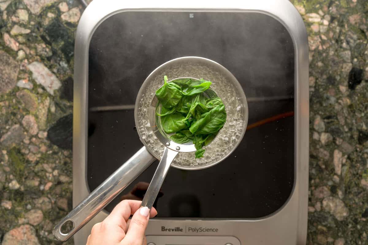 Overhead view of basil being blanched in boiling water.