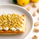 Closeup shot of basil-lemon ricotta toast surrounded by lemons and pistachios.