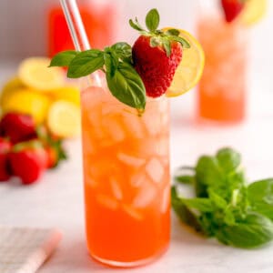 Glass of strawberry basil lemonade in front of a set scene.