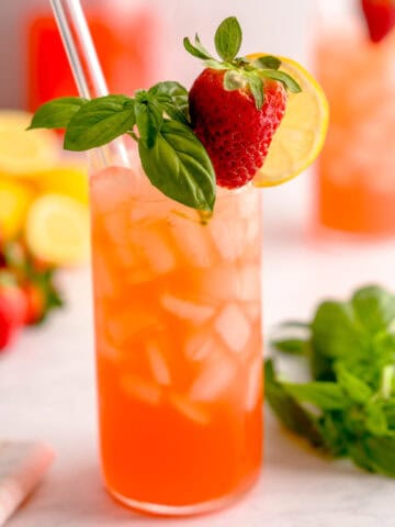 Glass of strawberry basil lemonade in front of a set scene.
