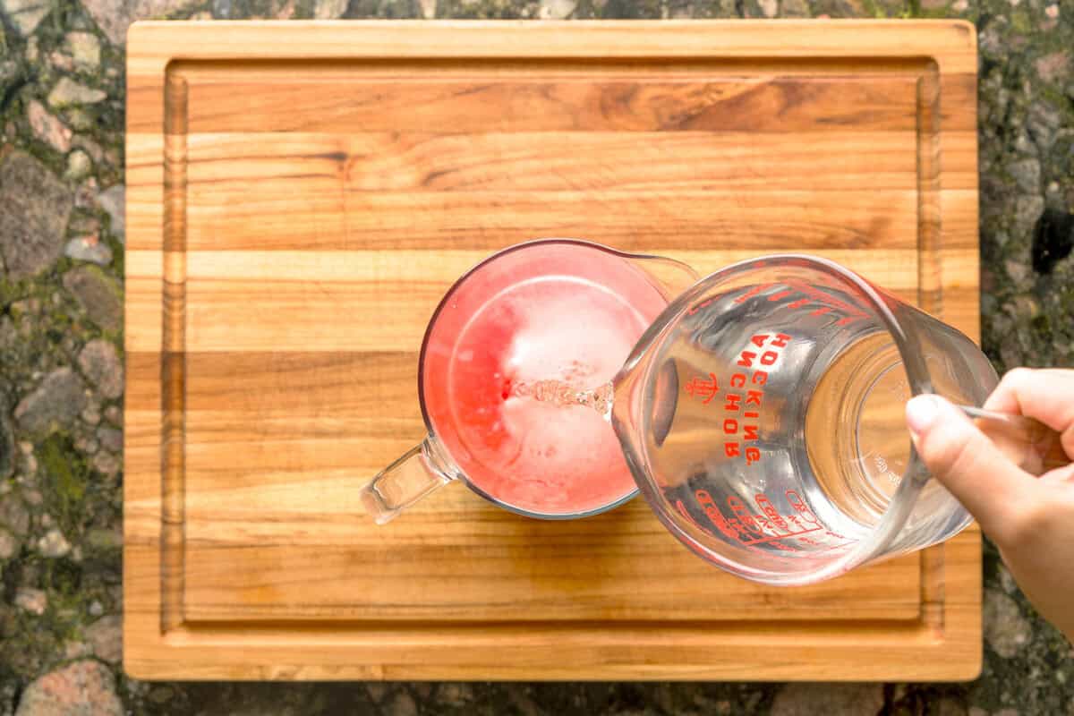 Overhead pour of water into strawberry basil lemonade pitcher.