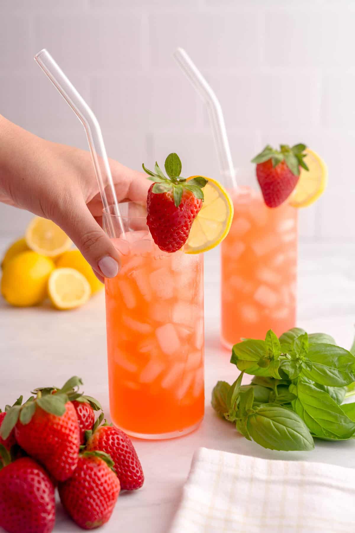 Two glasses of strawberry basil lemonade surrounded by lemons, basil and strawberries.