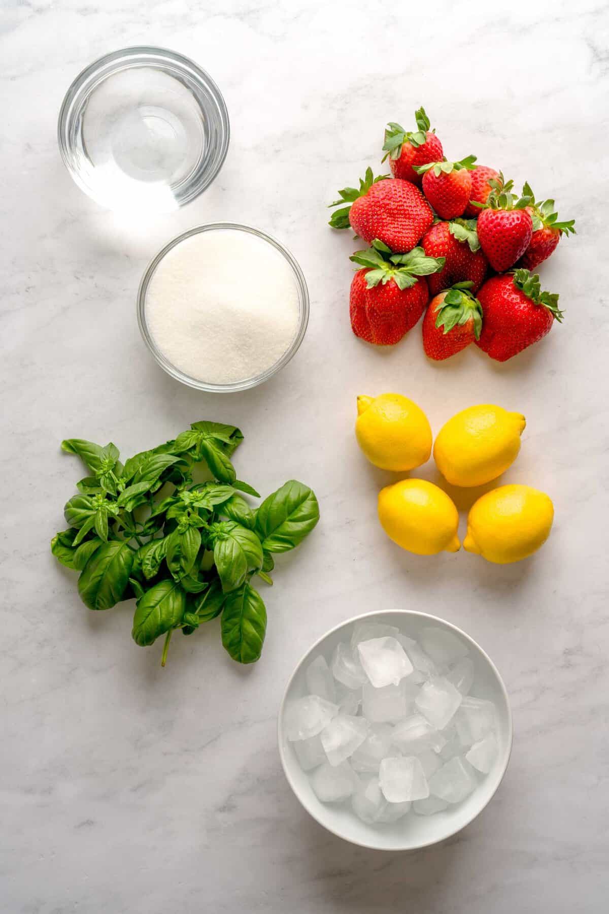 Overhead shot of ingredients to make Italian strawberry basil lemonade, including lemons, basil, strawberries, water, ice and sugar.