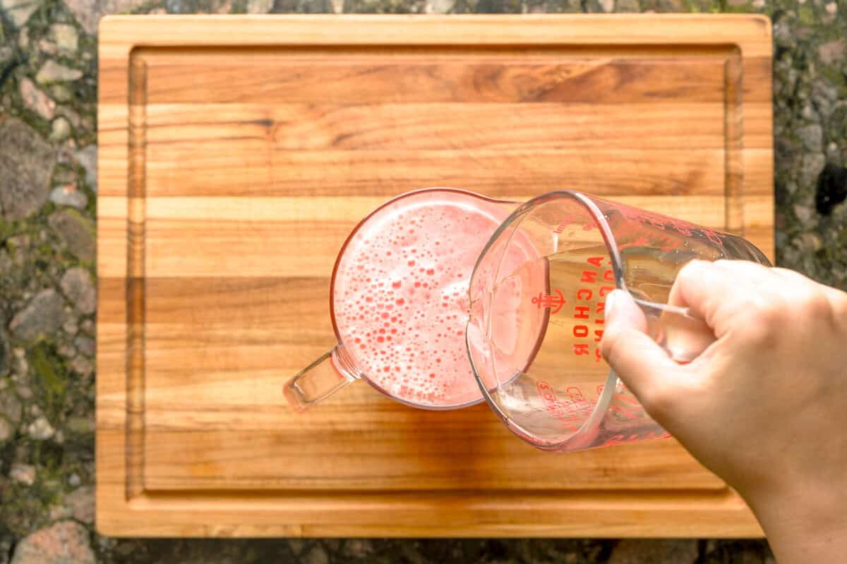 Overhead shot of a pour of basil simple syrup into a pitcher of strawberry lemonade.
