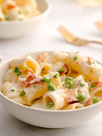 Bowl served with easy creamy pasta with parmesan, peas and prosciutto.