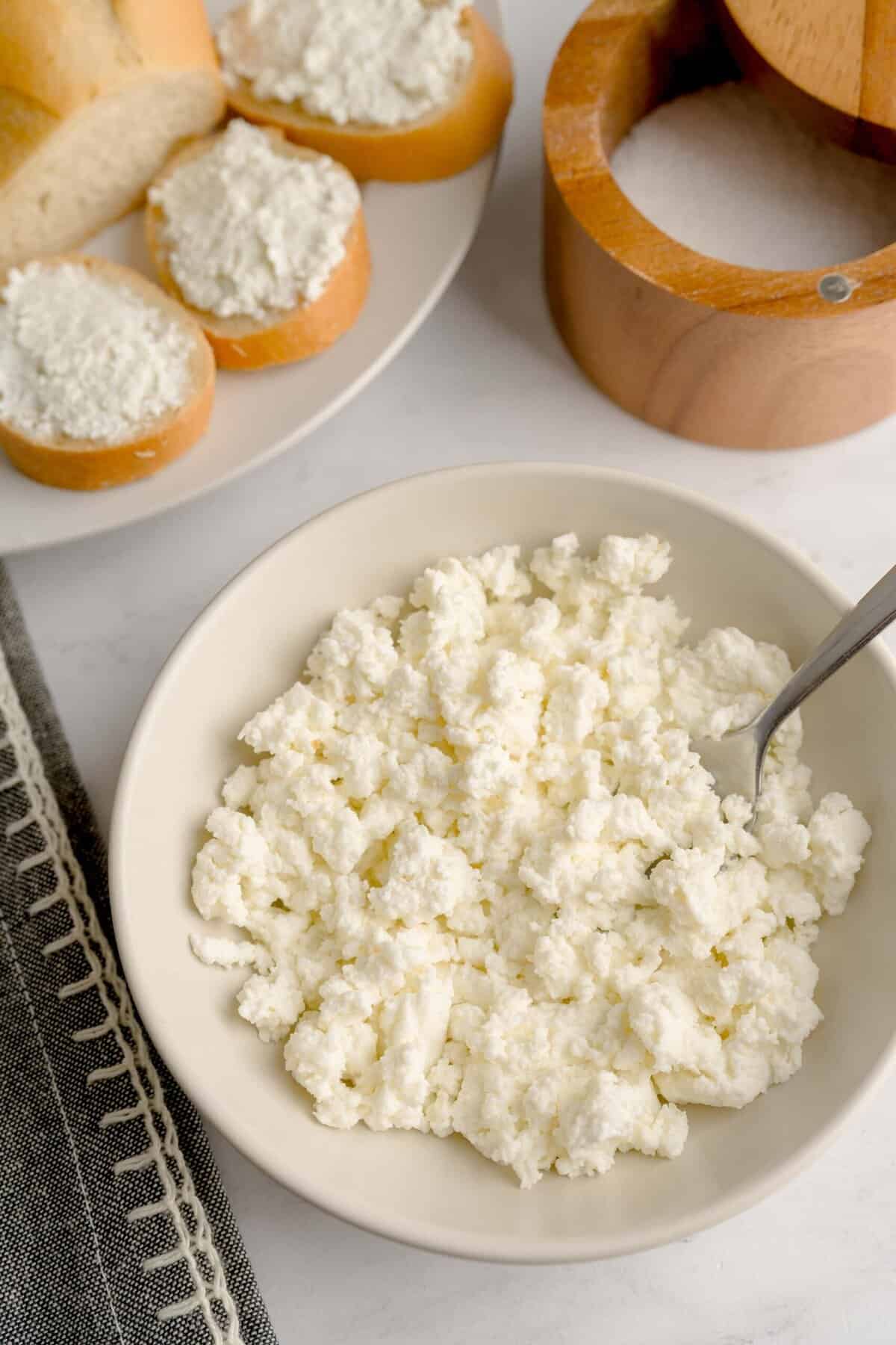 Overhead shot of set scene homemade ricotta cheese next to slices of bread with ricotta spread.