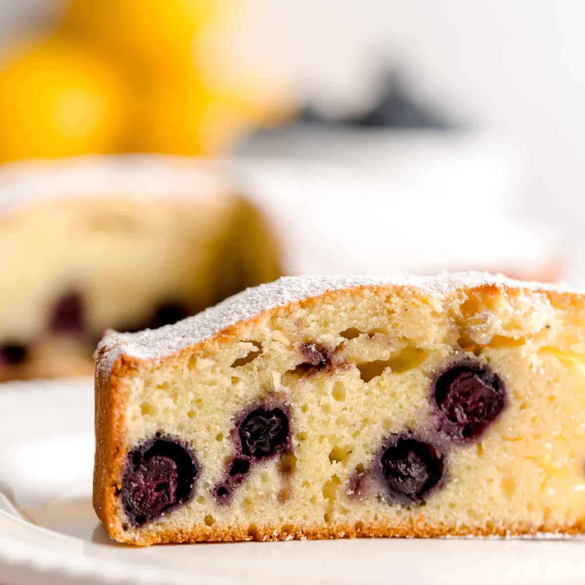Slice of lemon blueberry olive oil cake dusted with powdered sugar, showing juicy whole blueberries.