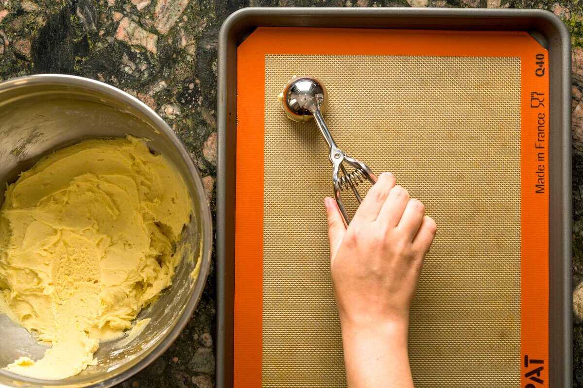Scooping lemon ricotta cookie dough onto a baking sheet.