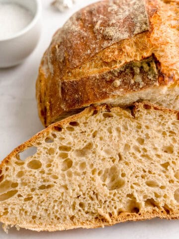 A slice of homemade Italian bread in front of a half loaf.