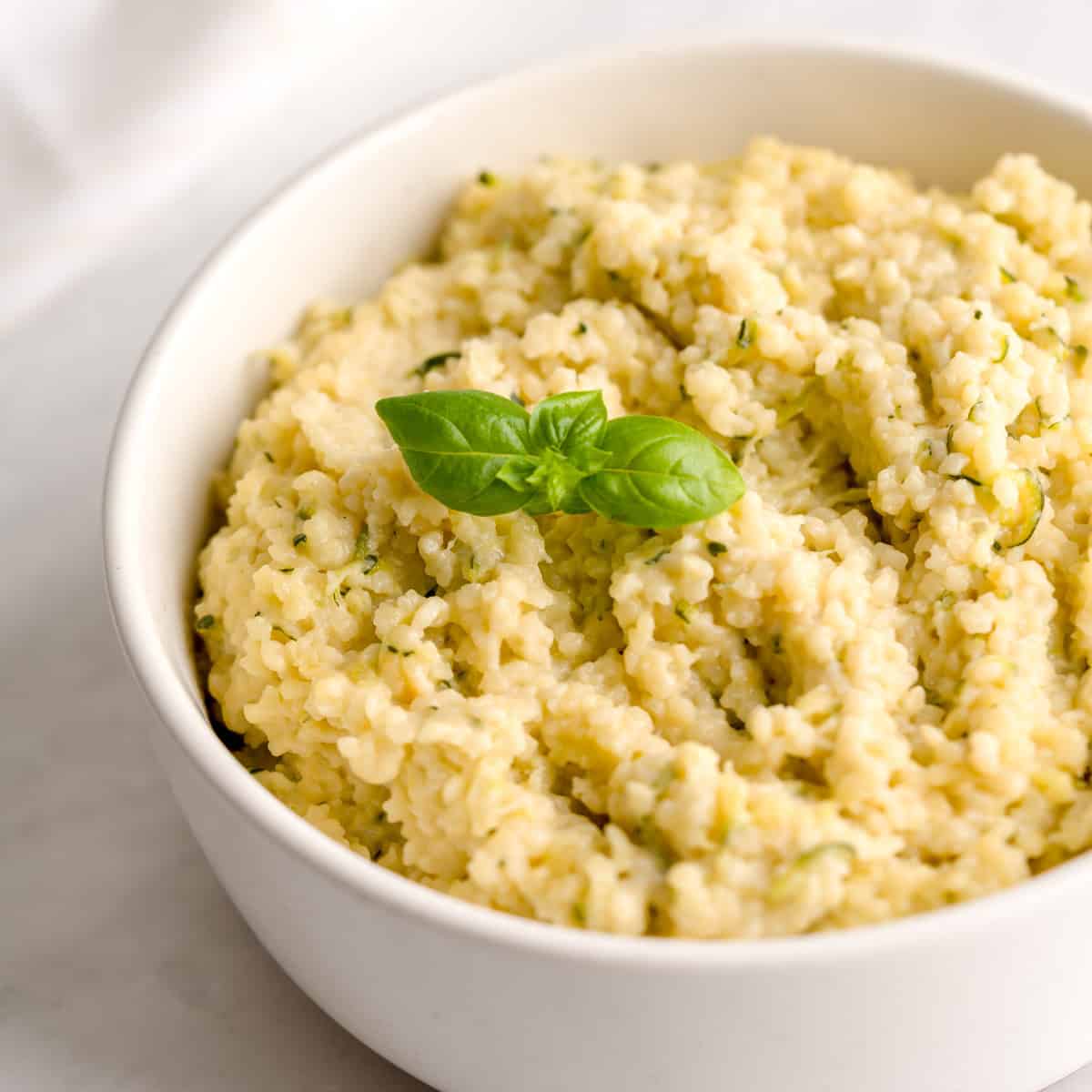 Creamy zucchini pastina served in a white bowl, garnished with a fresh basil leaf.
