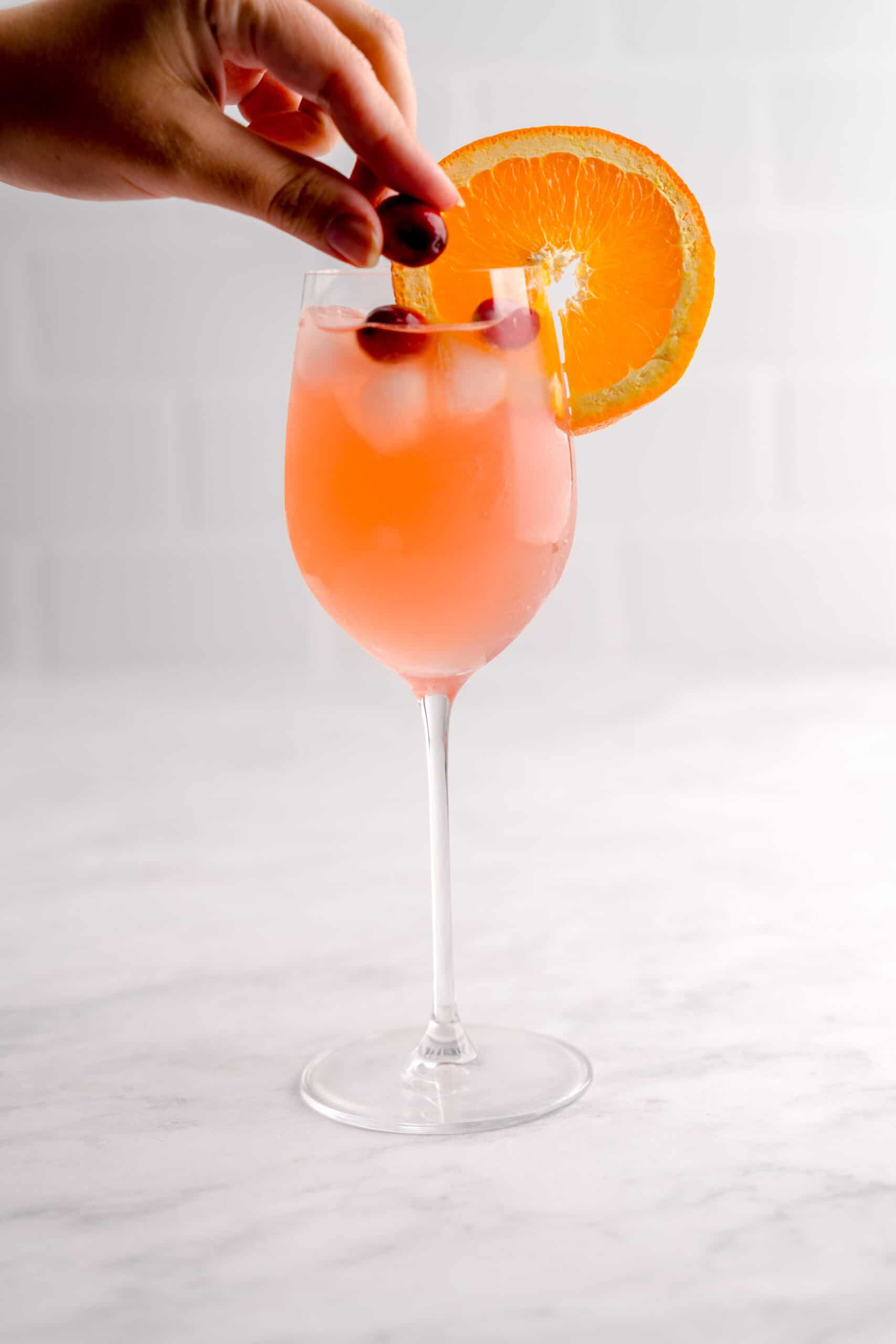 Hand over cranberry aranciata spritz garnishing the drink with fresh cranberries.