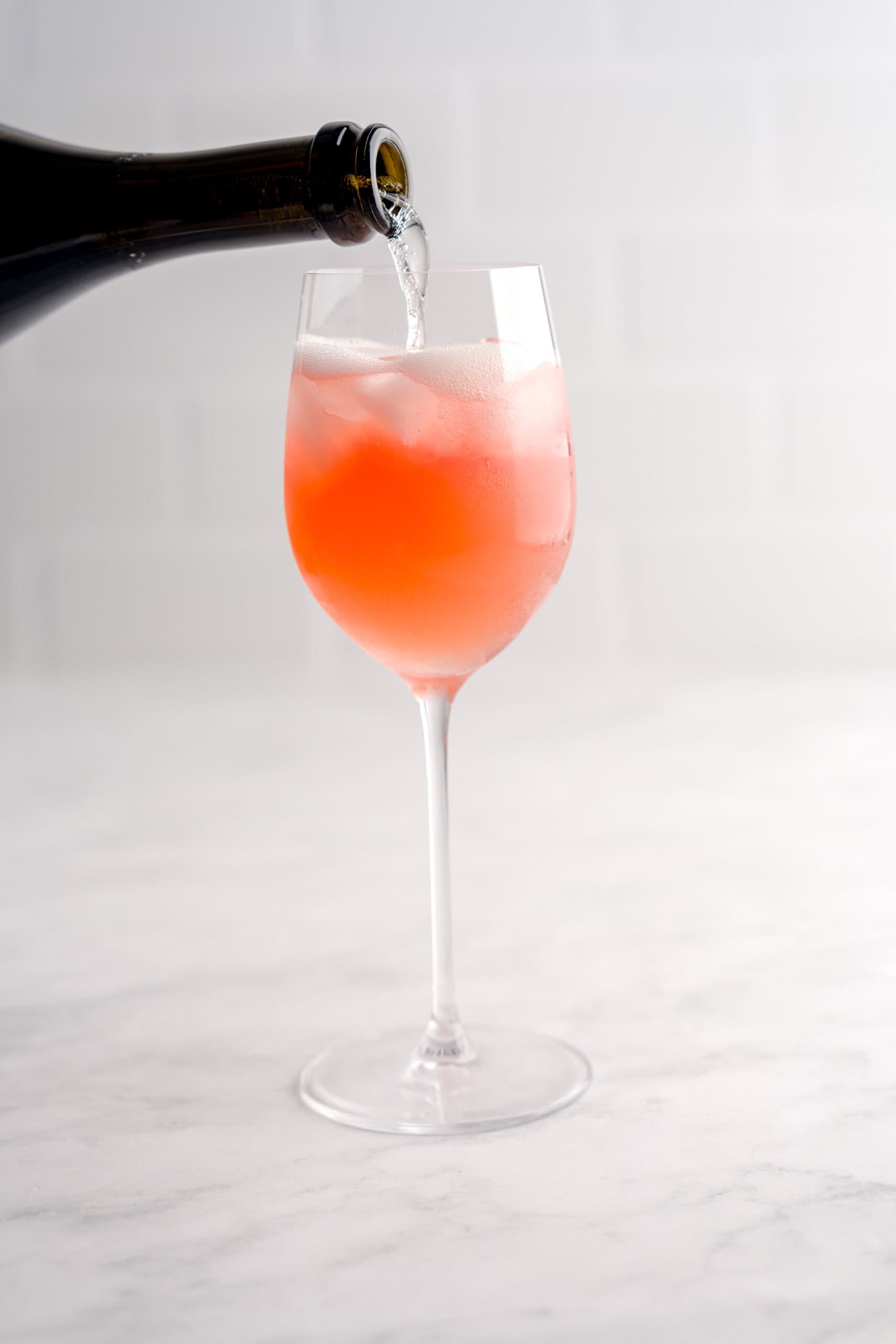 Pouring prosecco over an Italian-inspired cranberry aranciata spritz cocktail.