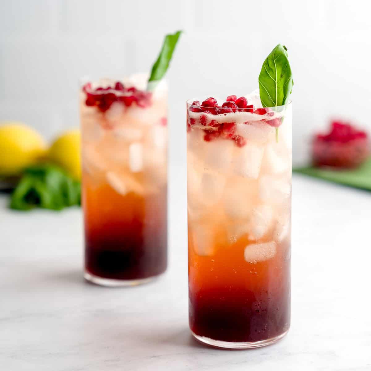 Two glasses of pomegranate basil fizz garnished with pomegranate seeds and fresh basil 