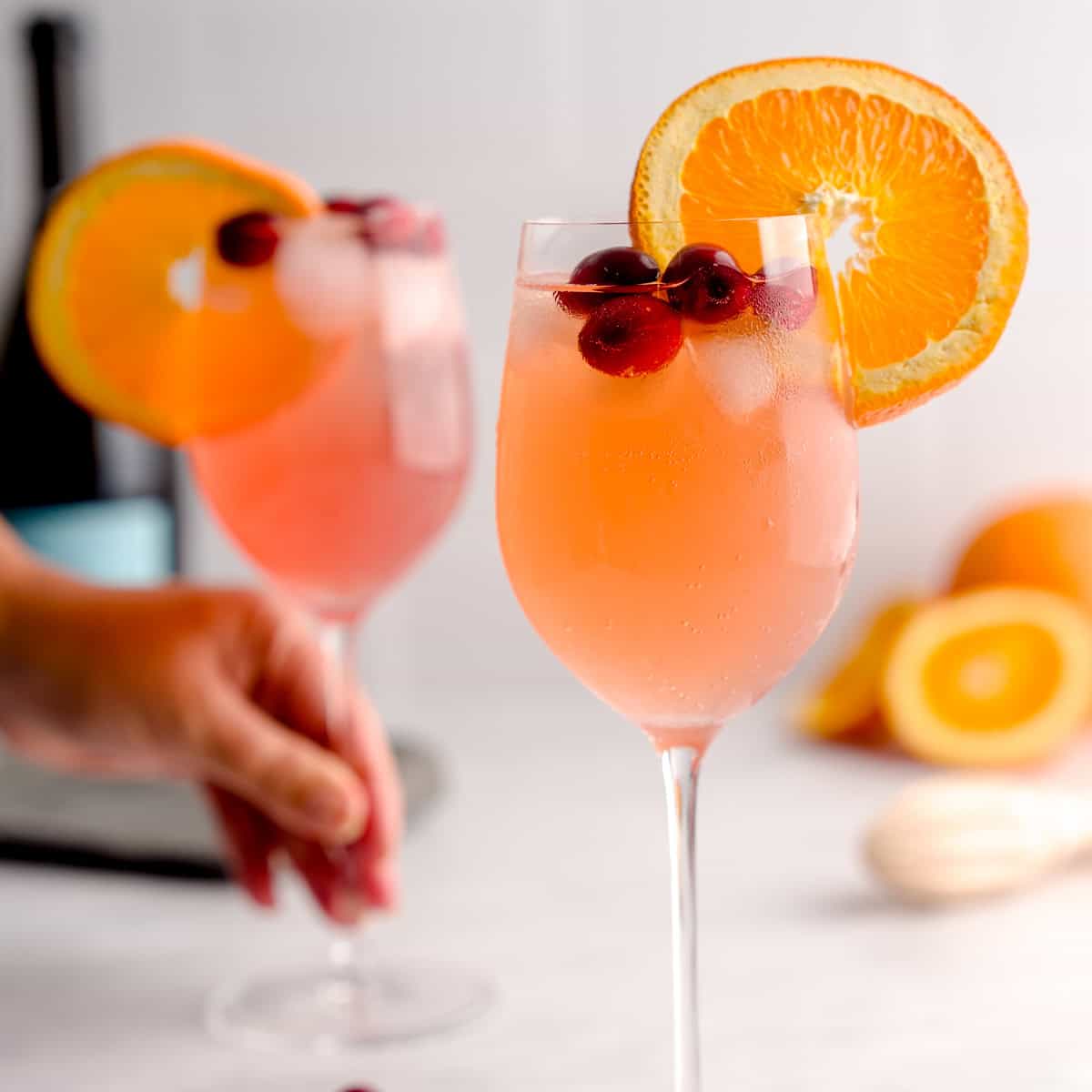 Two glasses of Cranberry Aranciata Spritz garnished with orange slices and cranberries on ice.