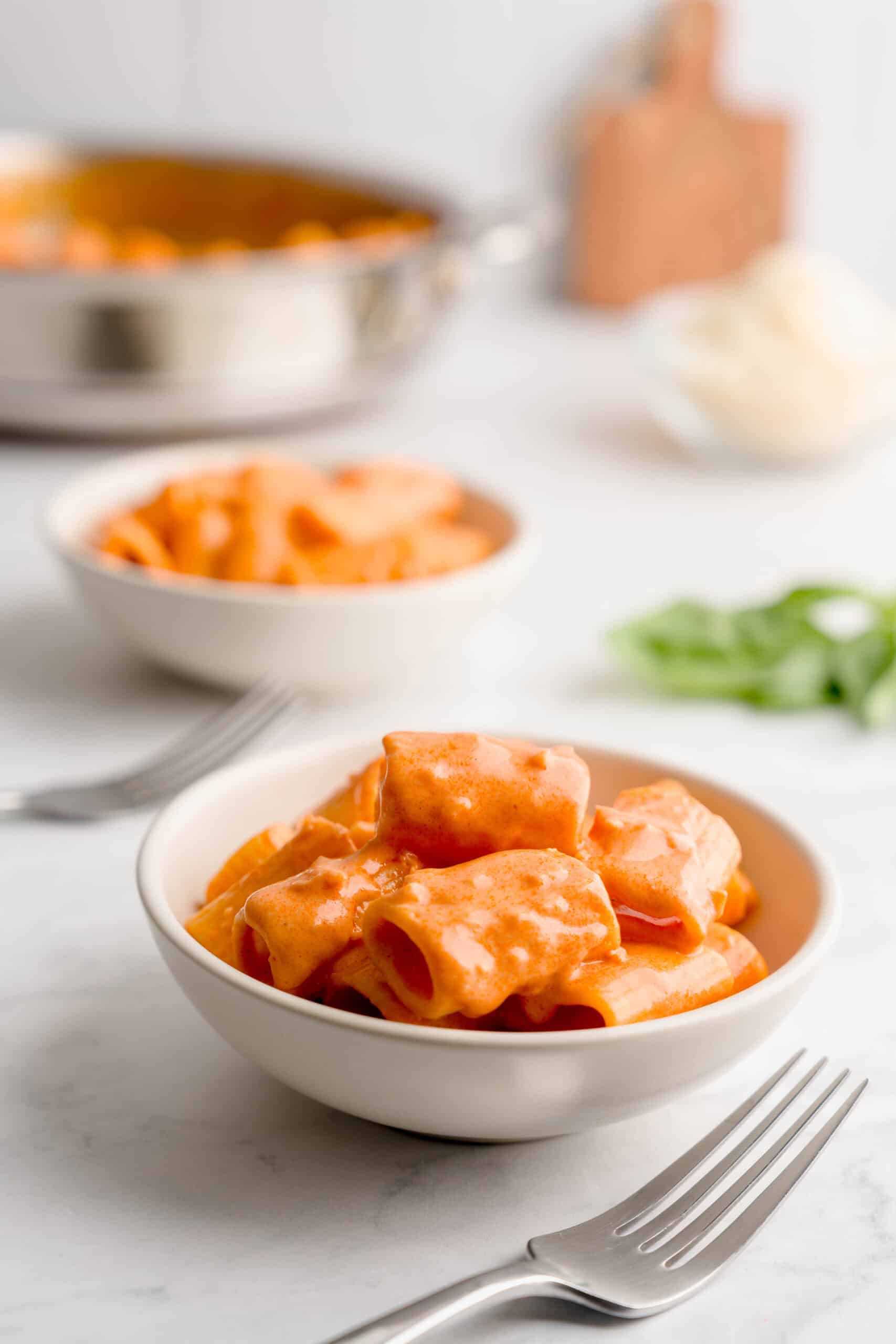 Two bowls of creamy vodka pasta with two forks in a set scene.