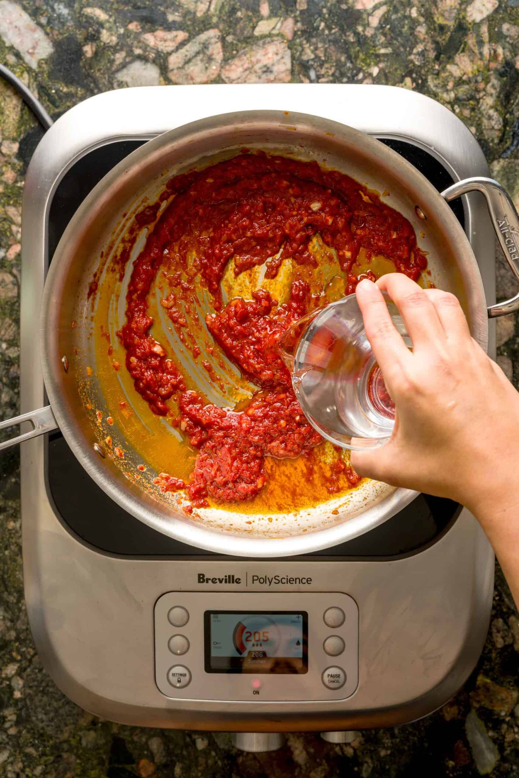 Pouring vodka into pan to make creamy vodka pasta sauce.