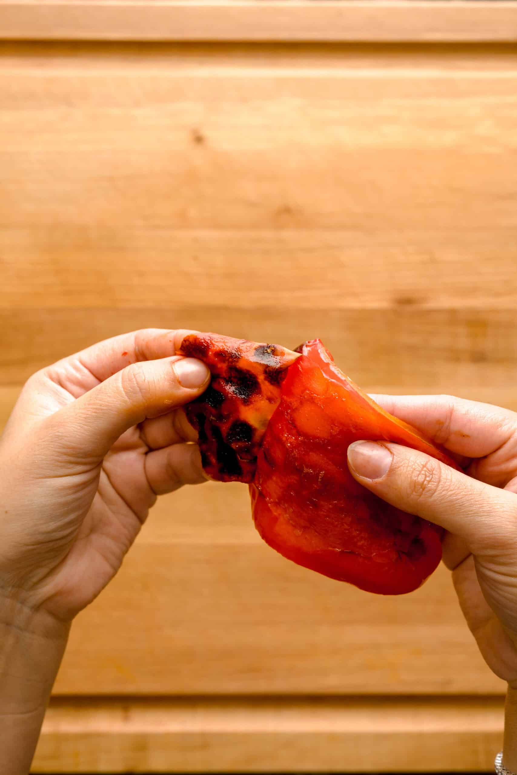 Hands peeling charred skin from a roasted red pepper.