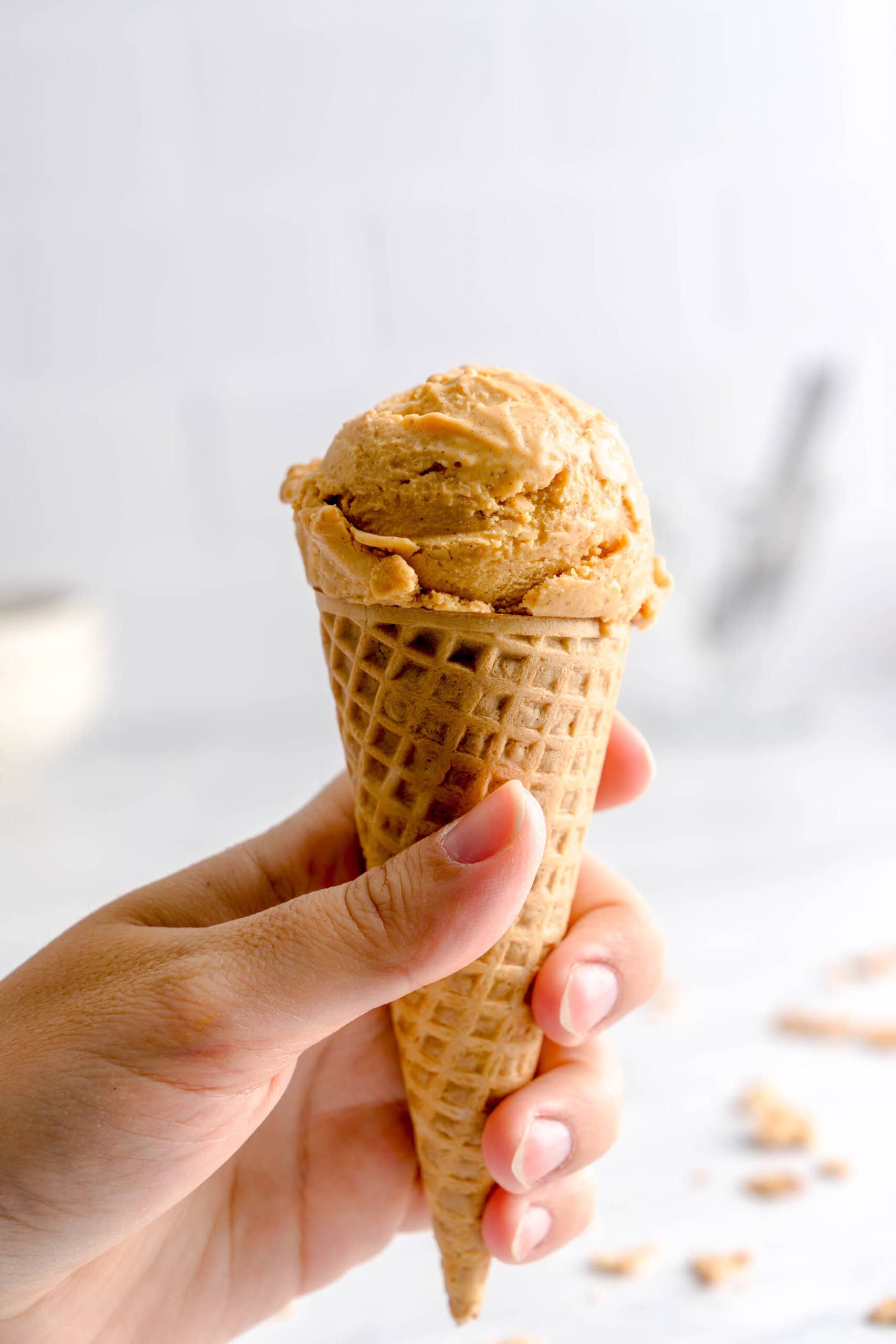 Hand holding a waffle cone topped with a ball of pumpkin spice gelato.