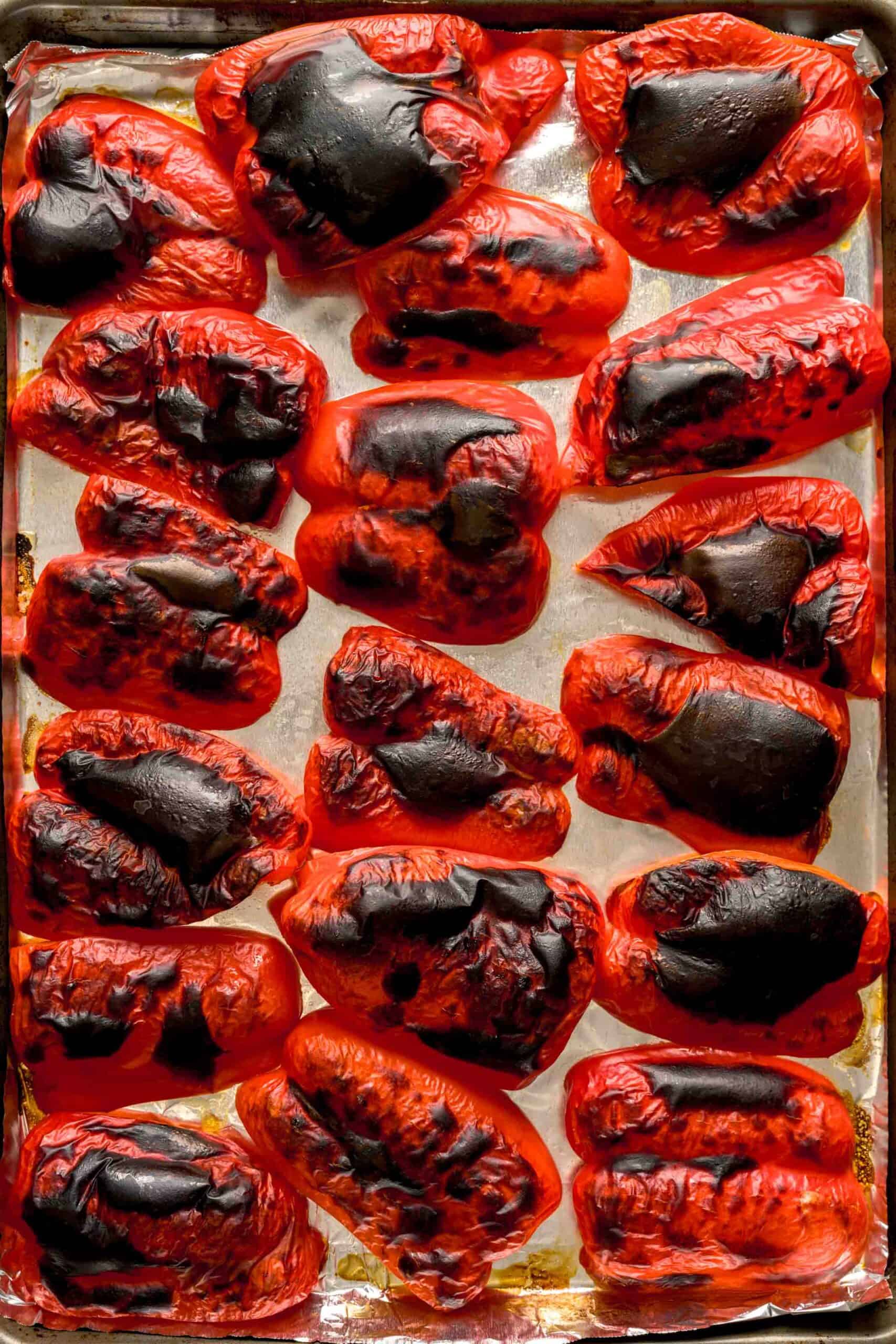 Charred red peppers above an aluminum foil-lined baking tray.