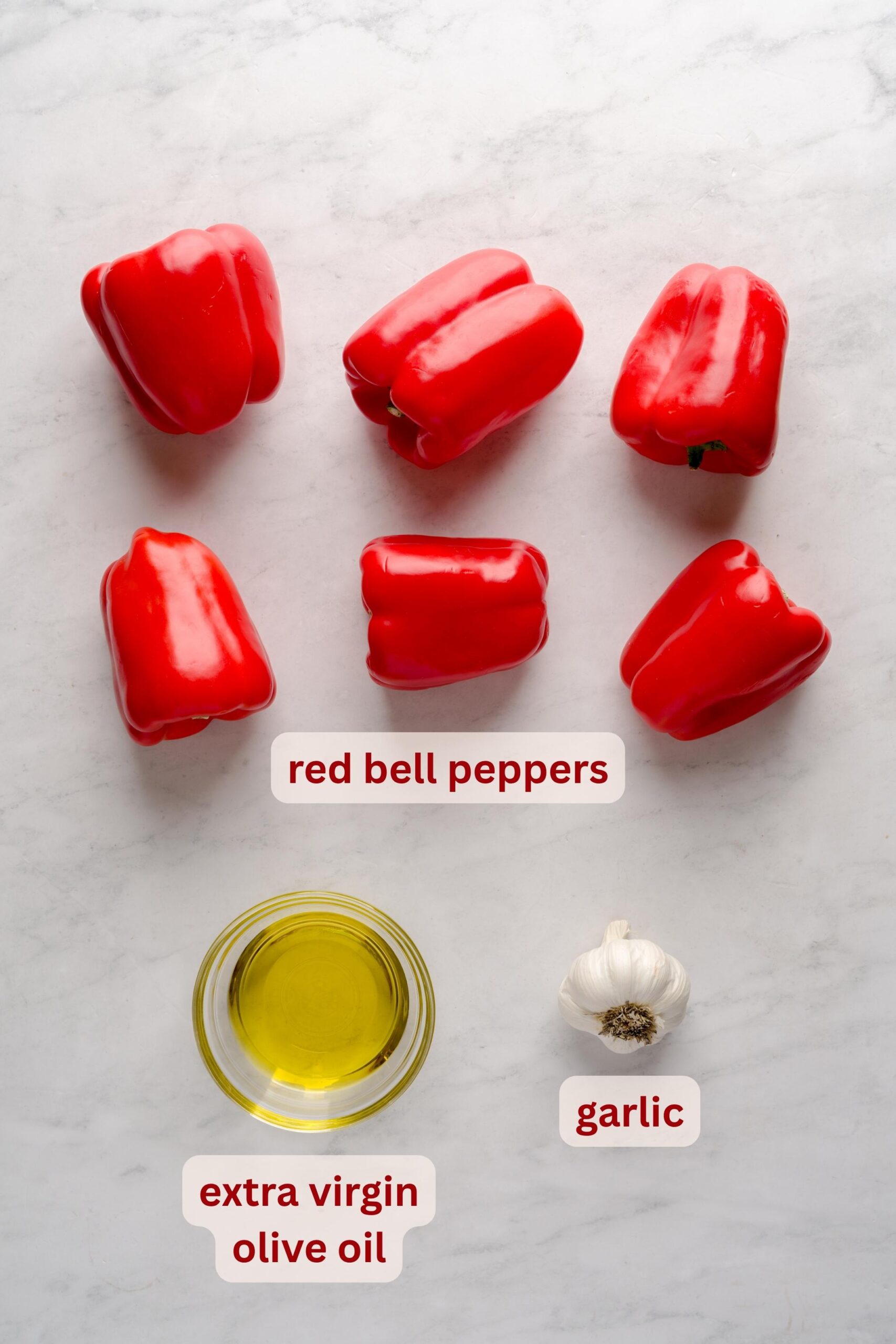 Red bell peppers, garlic, and olive oil on a white surface.