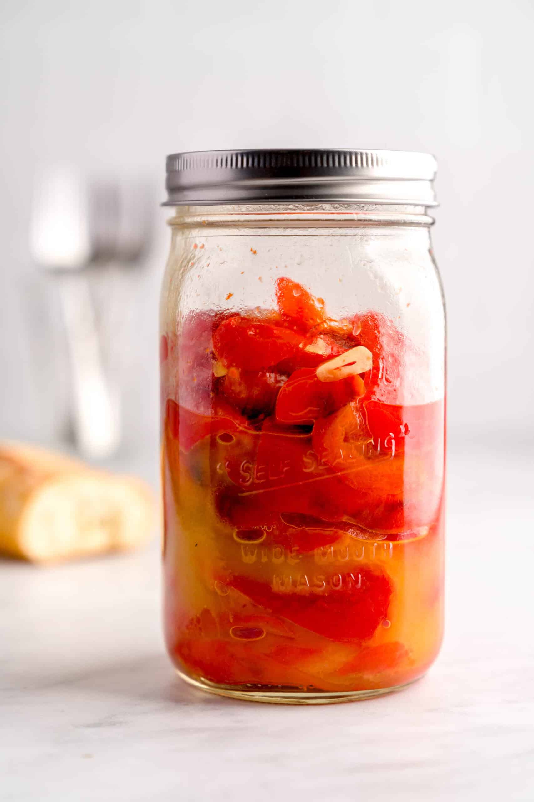 Italian roasted red peppers in a jar with olive oil and garlic slices.