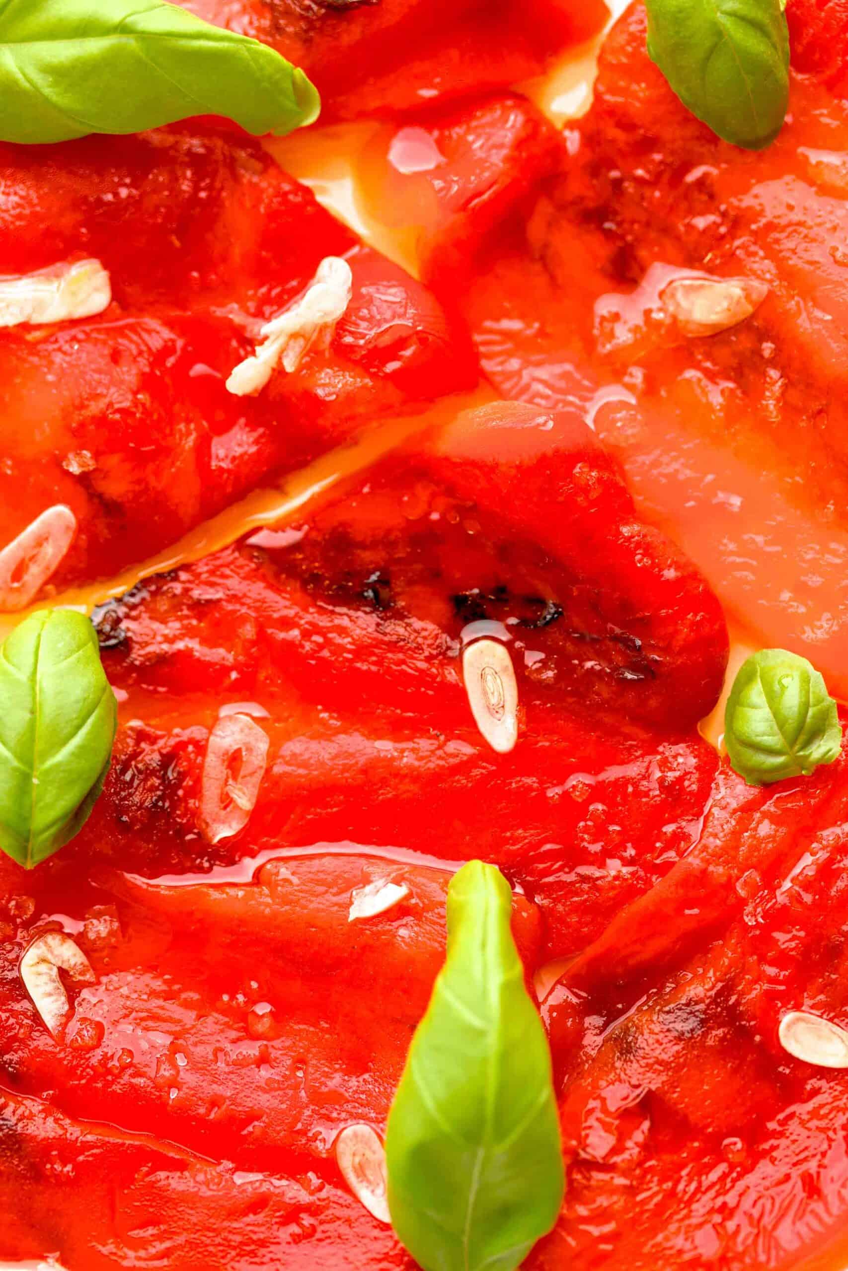 Close up shot of sliced roasted red peppers drizzled with olive oil, flaky salt and basil leaves.