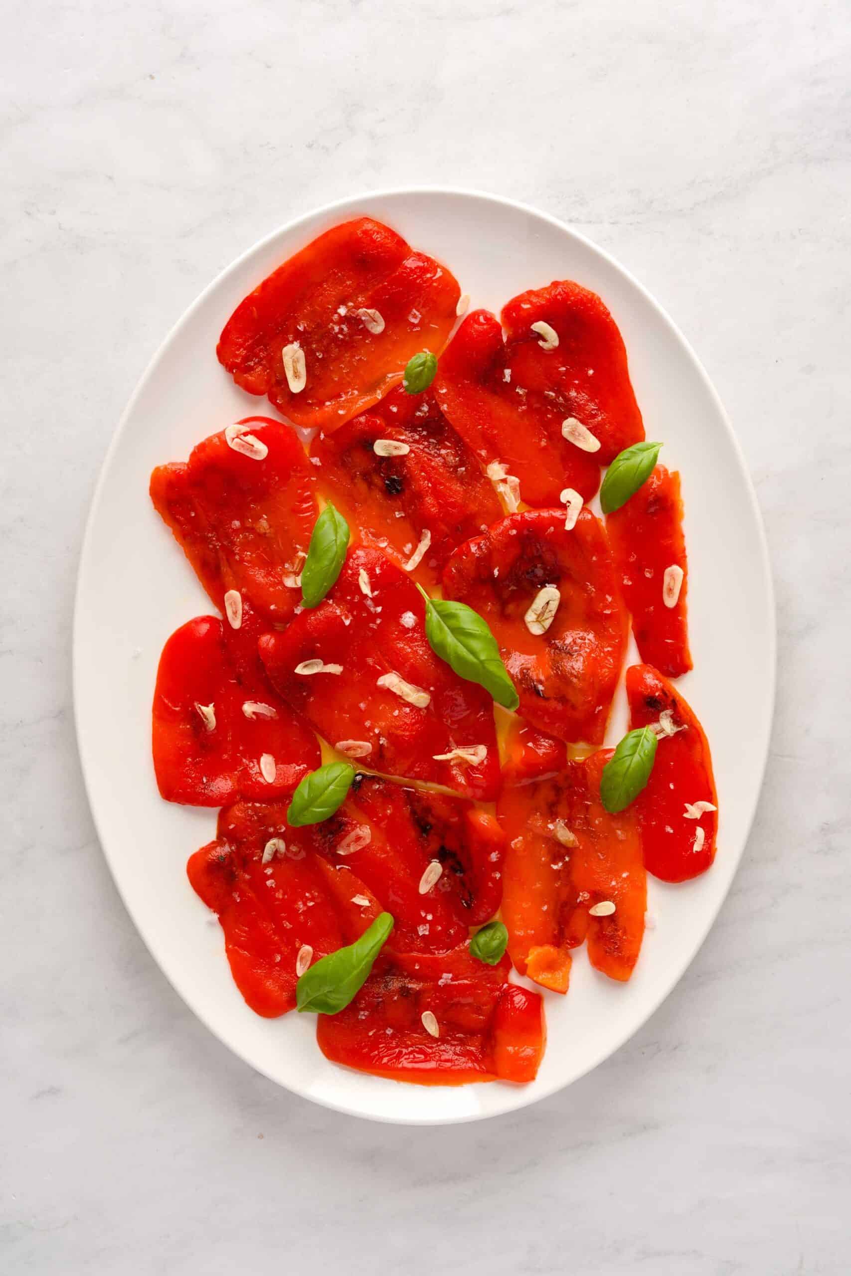Slices of roasted red peppers on a plate served with basil, olive oil and sliced garlic.